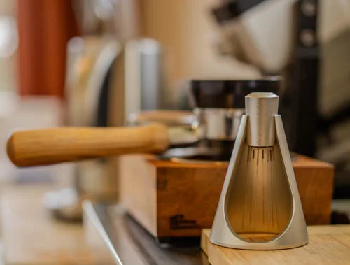 Sworksdesign WDT tool in its stand on a wooden bench, with a portafilter and espresso grinder behind