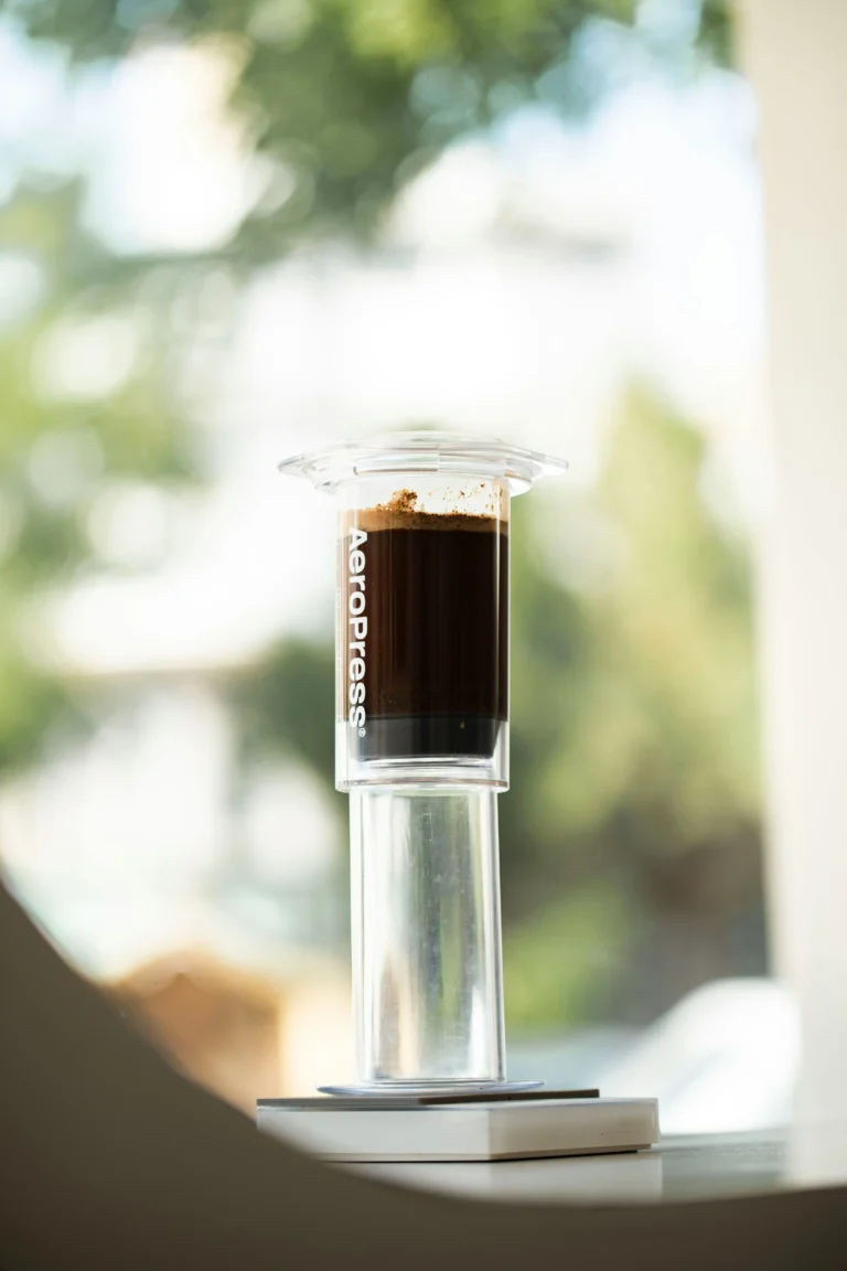 AeroPress full of brewing coffee, standing on a small scale by a sunny window